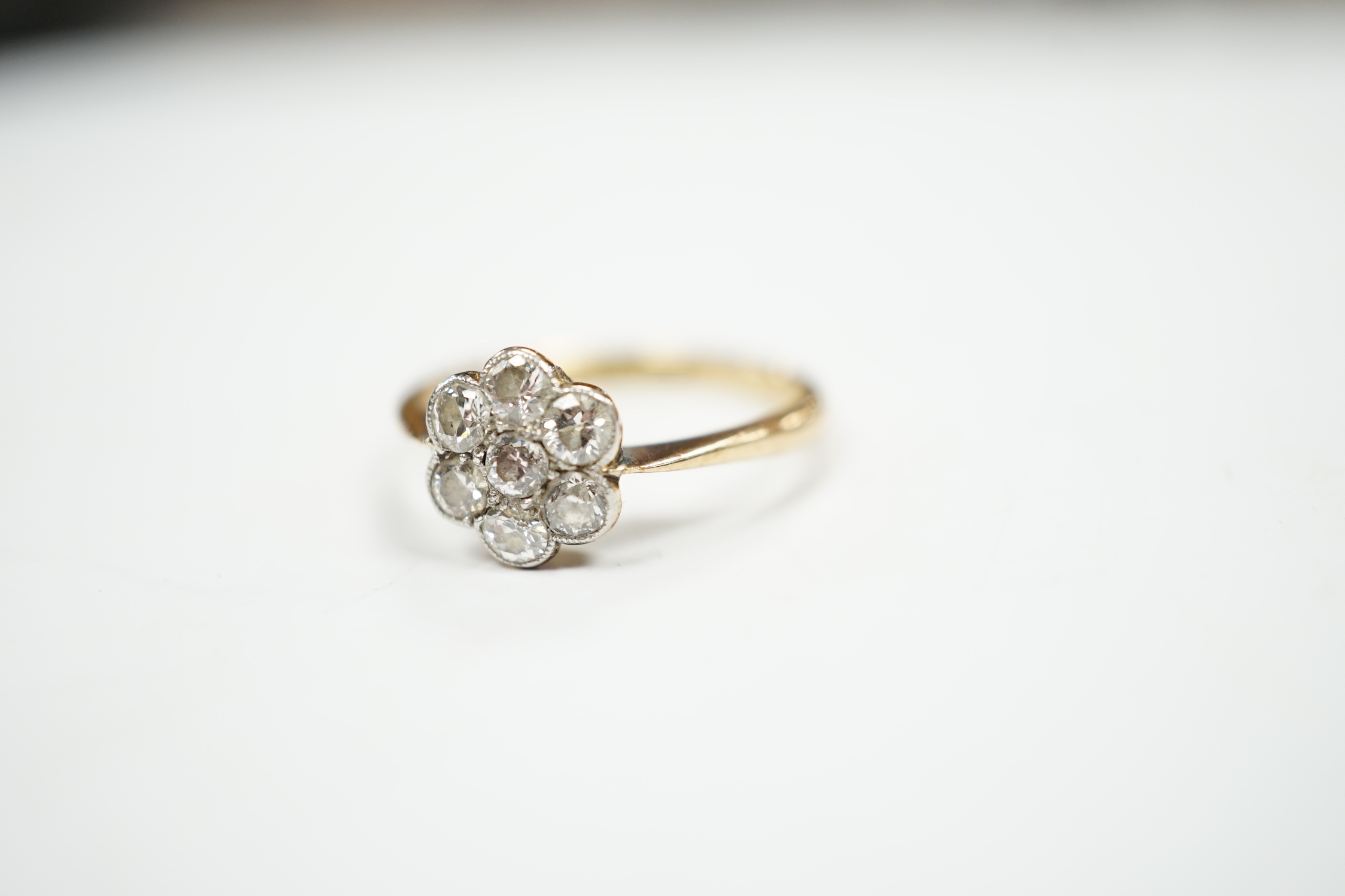 An 18ct and seven stone diamond set flower head cluster ring, size M/N, gross weight 2.9 grams.